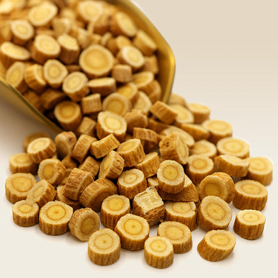 Dried Astragalus Root pieces spilling out of a gold scoop on a white background