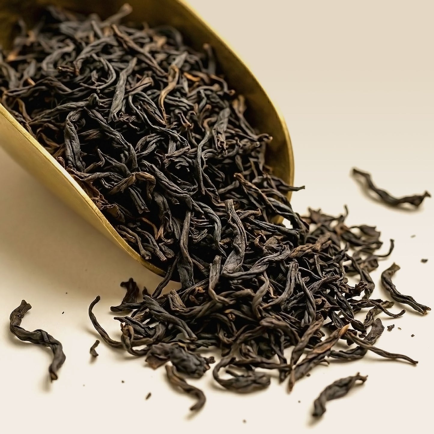 Dry ceylon black tea leaves in a gold scoop on a white background
