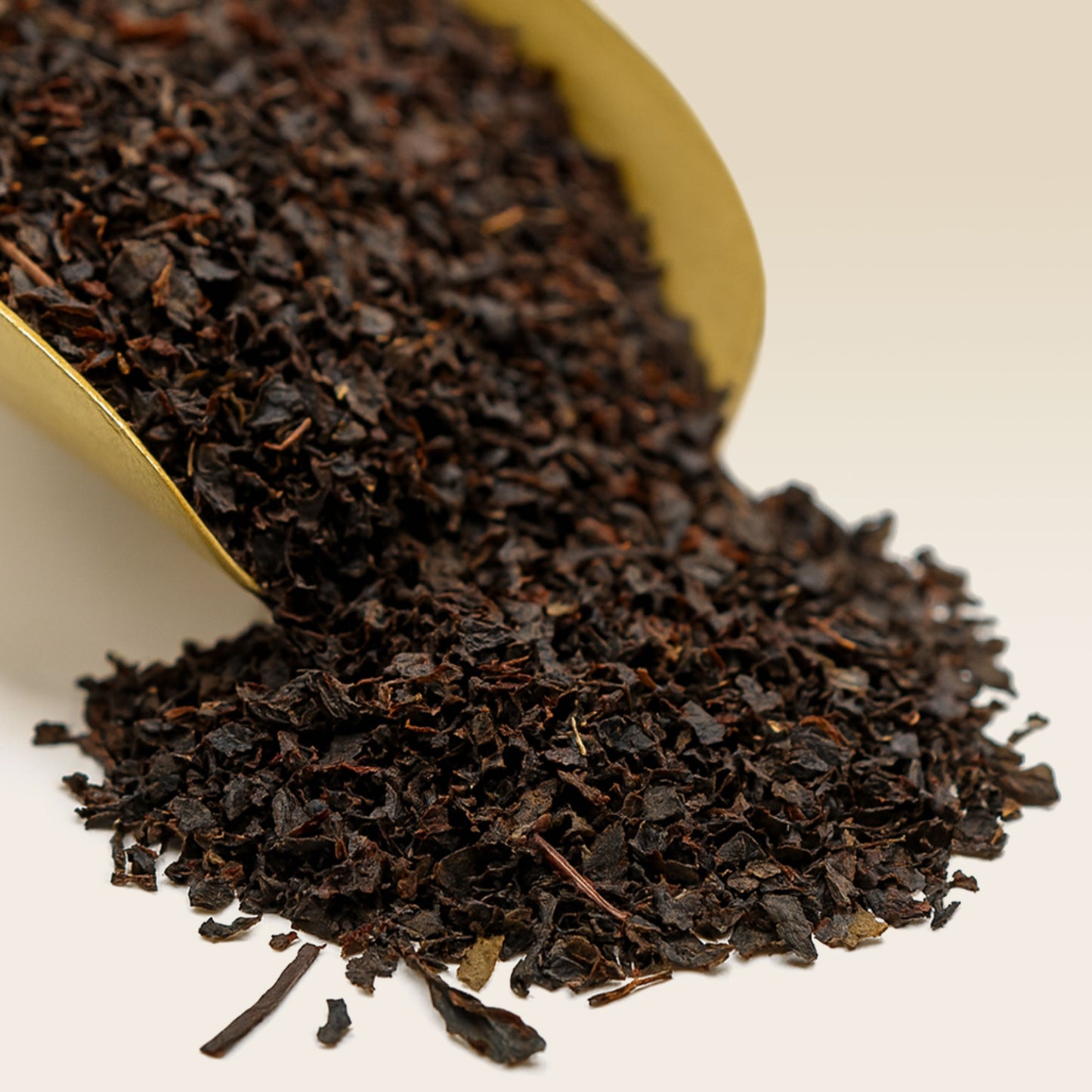 Dry black Daintree tea leaves in a gold scoop on a white background