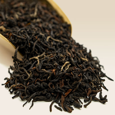 Close-up of Darjeeling black tea leaves with a wooden scoop on a white background