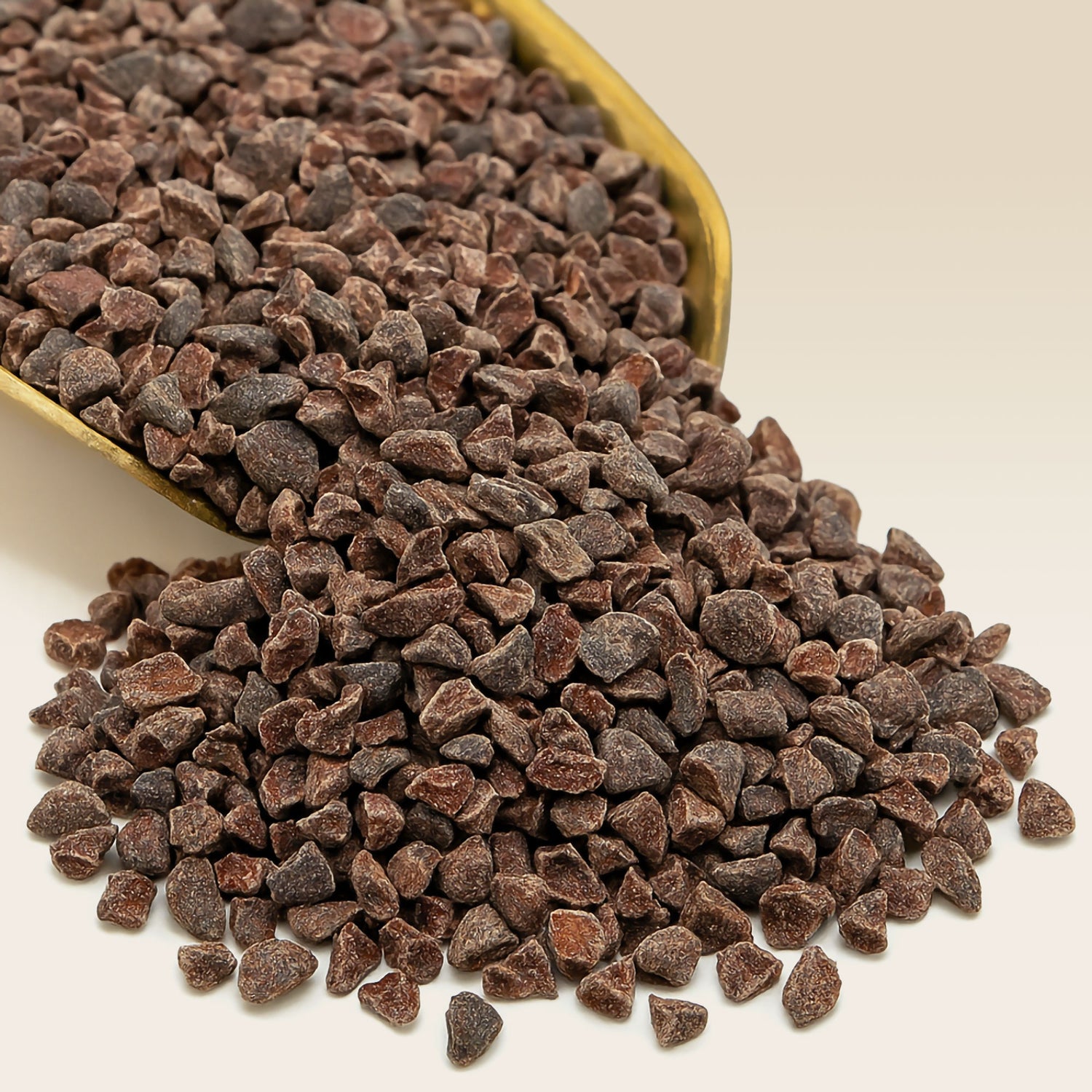 Chocolate cacco nibs spilling out of a container on a beige background