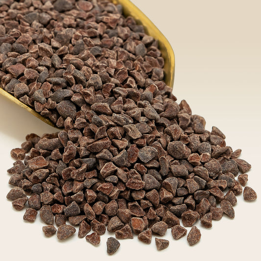 Chocolate cacco nibs spilling out of a container on a beige background