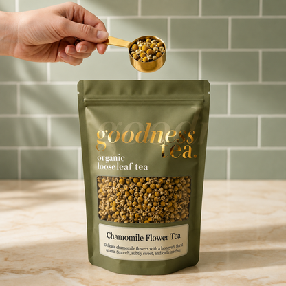 Goodness Tea package with chamomile flowers being measured with a spoon against a green tiled wall.
