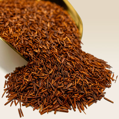 Close-up of dried red rooibos tea leaves spilling from a scoop.