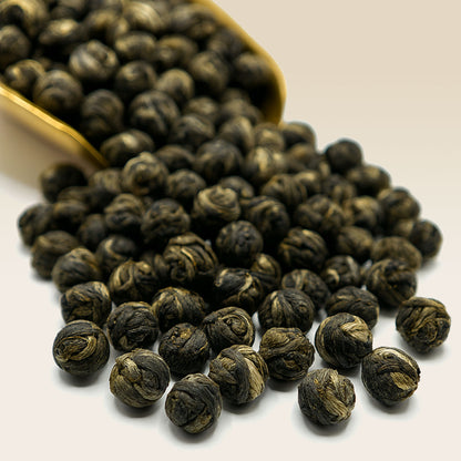 White Tea Jasmine Pearl Tea leaves spilling out of a gold scoop on a white background