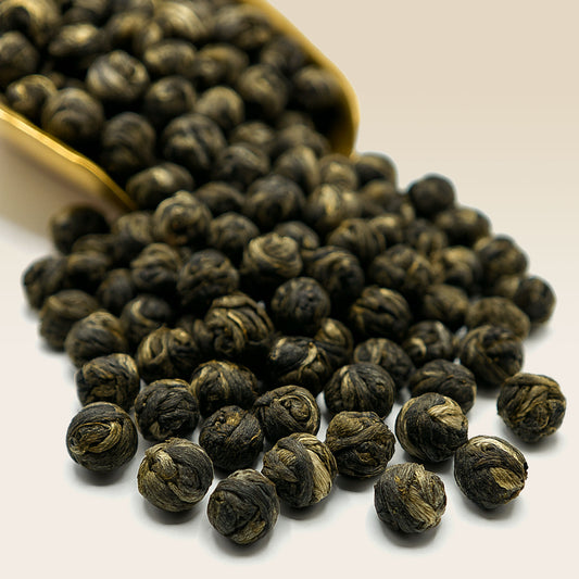 White Tea Jasmine Pearl Tea leaves spilling out of a gold scoop on a white background